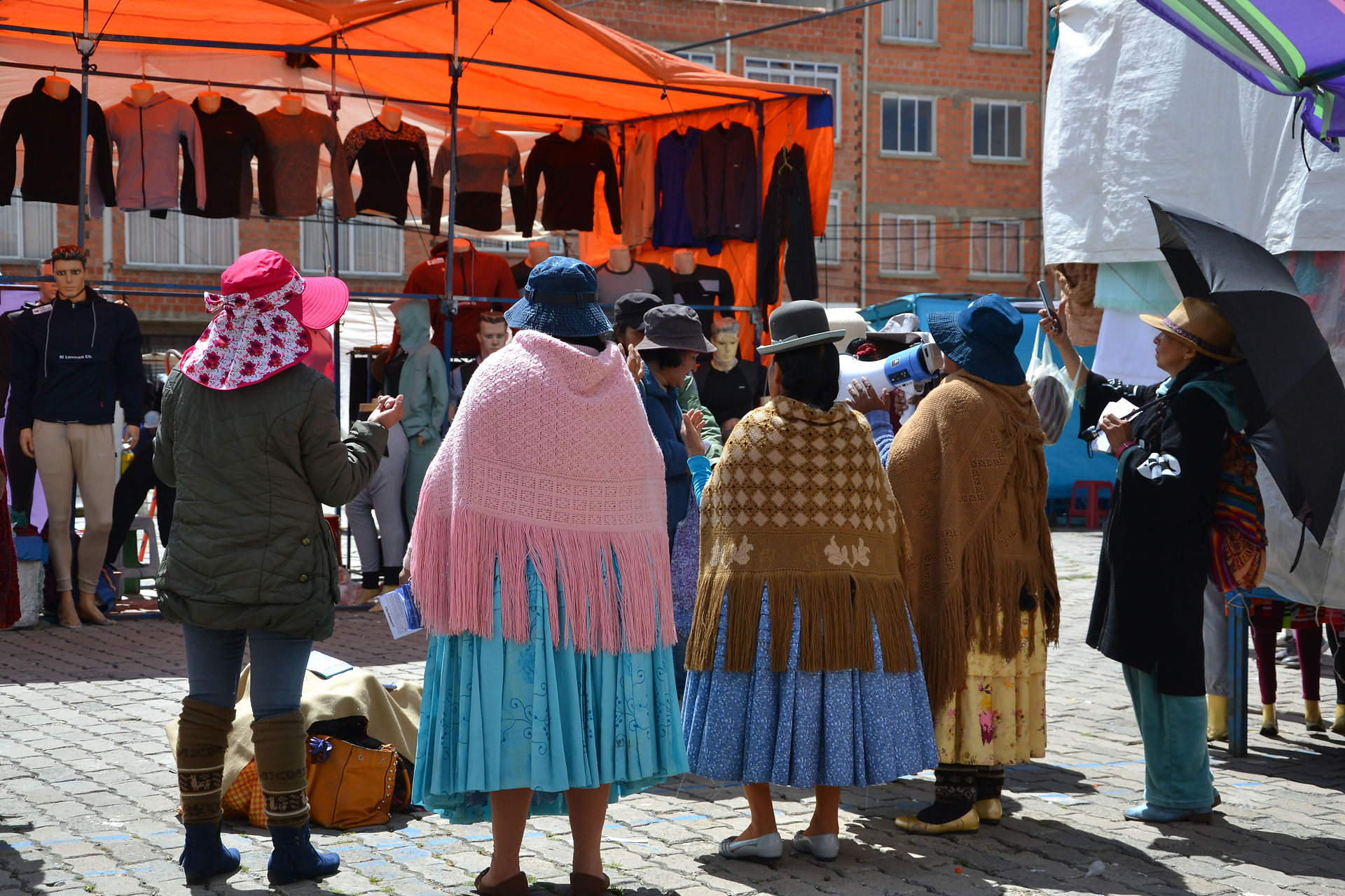 Three cholitas standing with their backs to preach at the El Alto market