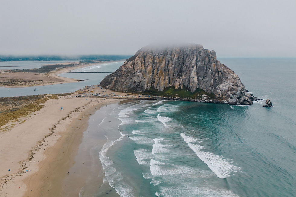 Aerial view of Morro Rock capped by marine-layer fog above the beach and harbor mouth