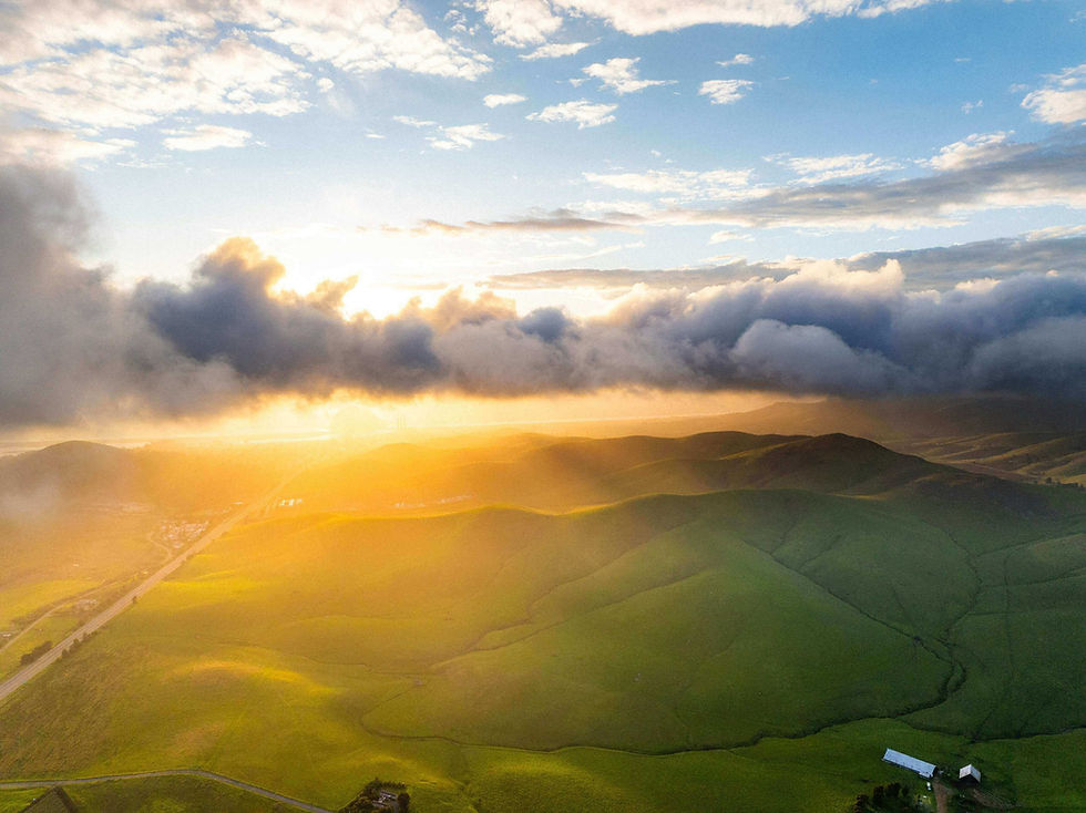 Morning sun breaking through clouds over green hills and a ranch