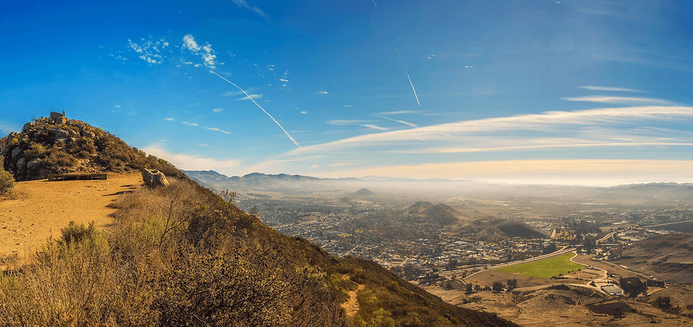 Neighborhoods spread across a valley below a dry hillside trail