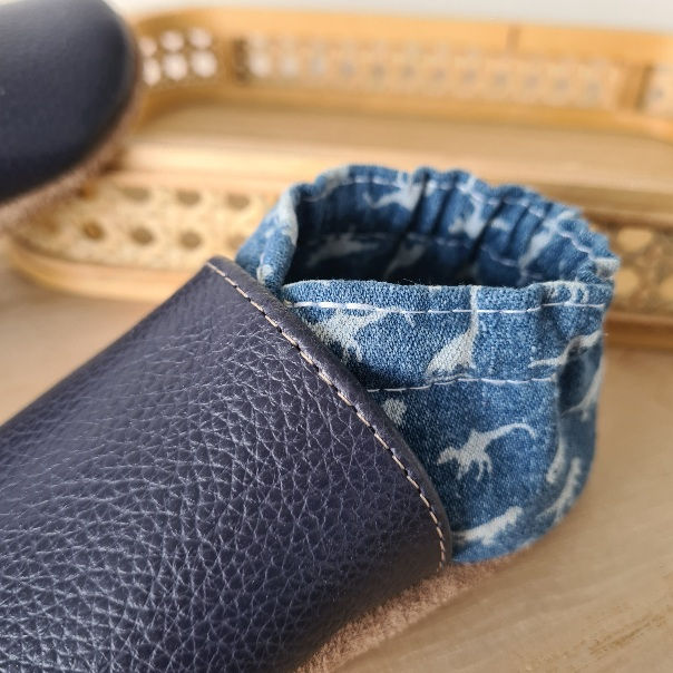 Miniature : Gros plan sur les motifs dinosaures et la texture du cuir souple bleu du modèle Pas de Dino.