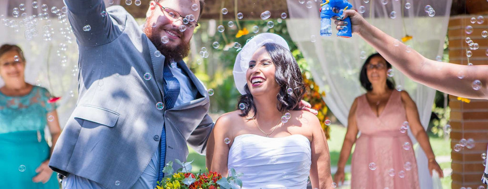noivo e noiva saindo da cerimônia sorrindo e se divertindo com as bolinhas de sabão que os convidados jogavam neles
