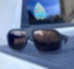 Sunglasses on a car roof reflect a house and person. Blue sky sticker reads "Haven." Mood is calm with neutral colors.
