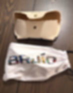 Beige canvas pouch with brass button and frayed edges sits above a white drawstring bag with colorful "BAJÍO" text on a wooden surface.