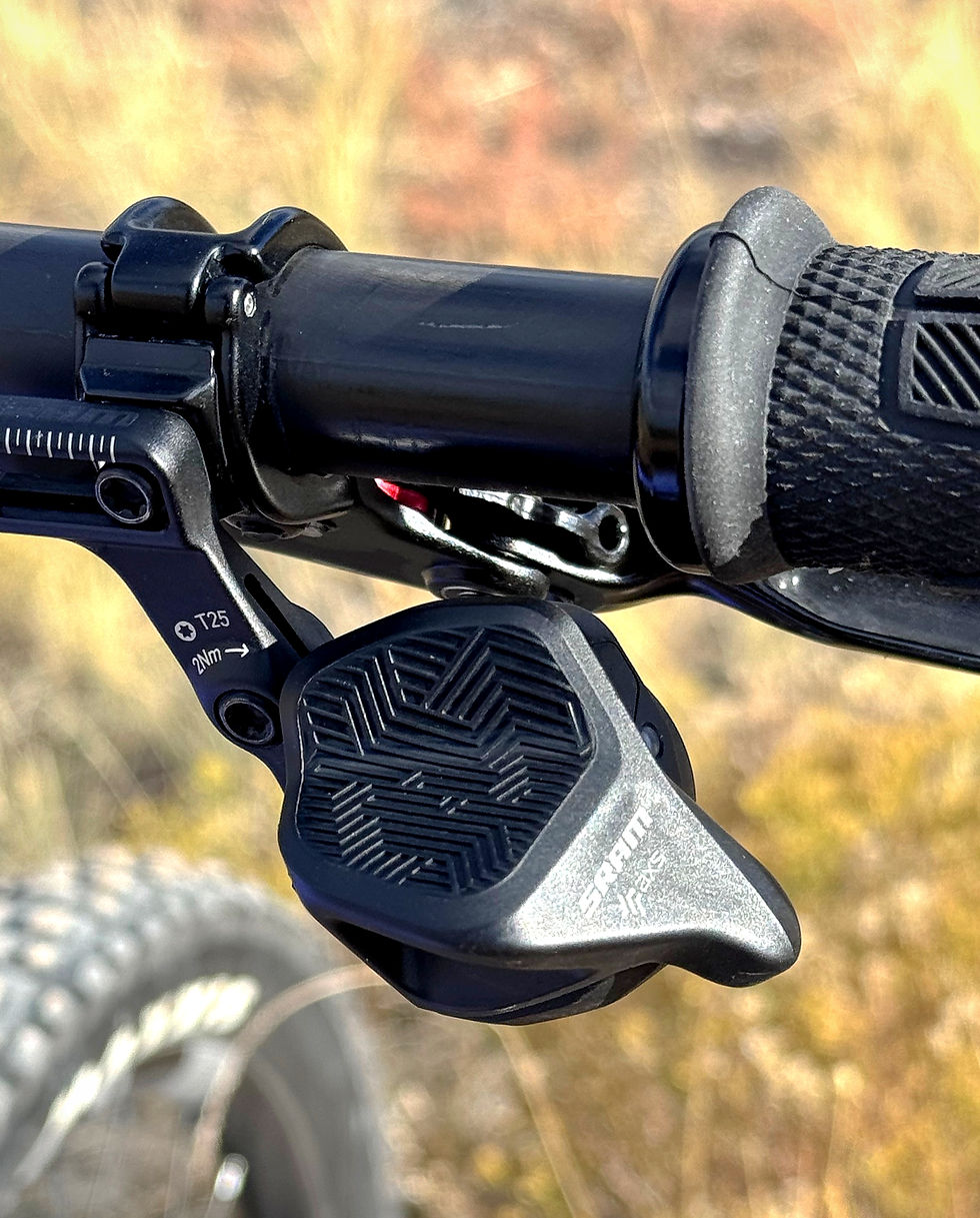 Close-up of a black bike handlebar with a textured grip and SRAM gear shifter. Handlebar is shown outdoors against a blurred natural background.