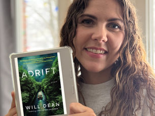 Books With Brittani smiles while holding an e-reader. On the e-reader, a mostly green book cover is shown, with the words "Adrift" and "Will Dean".