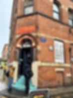 People in hoodies stand near a brick building with neon "Afflecks" sign. "Short Street" and "ARCANE" are visible. It's rainy and overcast.