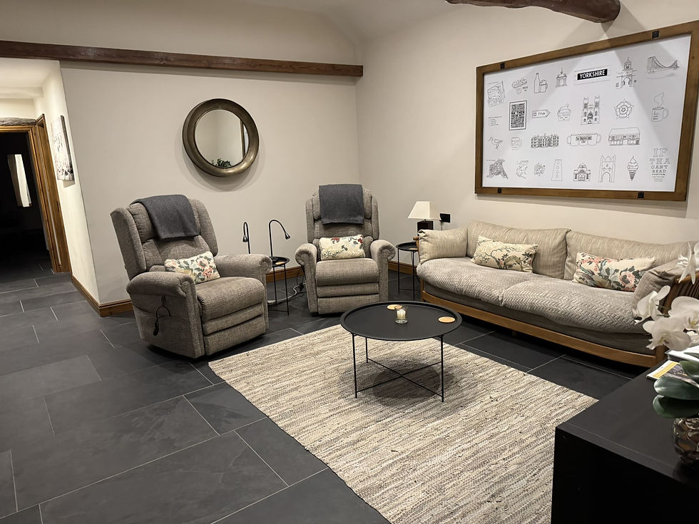 Cozy living room with two recliners, a sofa, and floral pillows. A round mirror and framed "Yorkshire" art on walls, soft lighting.