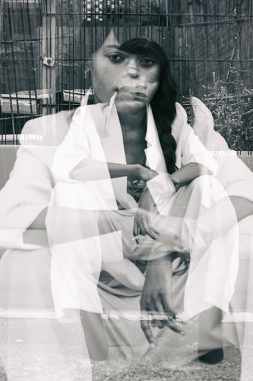 🔊 Alt Text:
A black-and-white image of a person seated low among dense plants with fabric draped around the body.