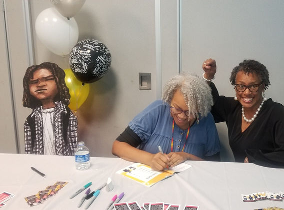 Female author signing book for her friend who is smiling and pointing at the author.