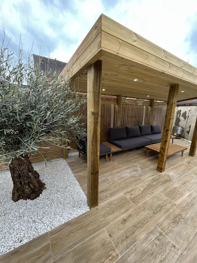 Olive tree with white gravel next to wood effect porcelain paving and timber pergola