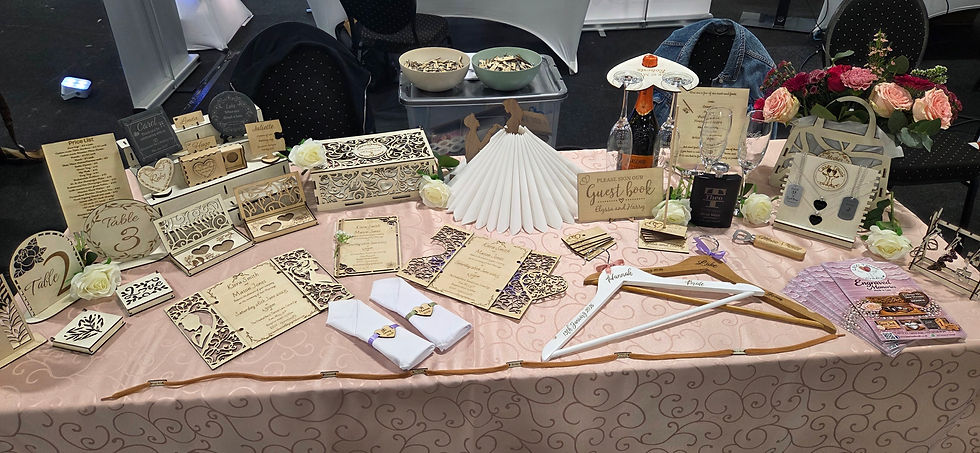 Display of elegant wedding decor items on a pink patterned tablecloth. Includes signs, invitations, flowers, and personalized hangers.