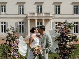 Couple de mariés devant une scénographie florale de mariage au Château de la Brulaire à Beaupréau, entouré de fleurs géantes en papier, de compositions florales, d'une décoration de cérémonie et d'une installation florale sur mesure. Inspiration de mariage haut de gamme réalisée par Loumer, studio floral durable spécialisé dans les fleurs en papier, les bouquets de mariée, les décors de cérémonie, les centres de table, les fleurs géantes, la location de décors floraux, l'installation de mariage, à Nantes, en Loire-Atlantique, dans le Maine-et-Loire et partout en France.
