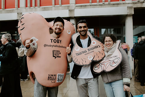Man in testicle suit poses with two people wearing 'talking bollocks' signs around their necks, shaped like testicles.