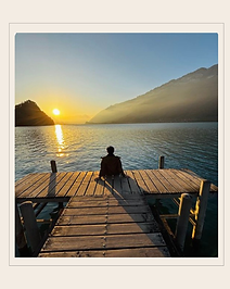 Uma pessoa sentada num deck observando o por do sol no mar.