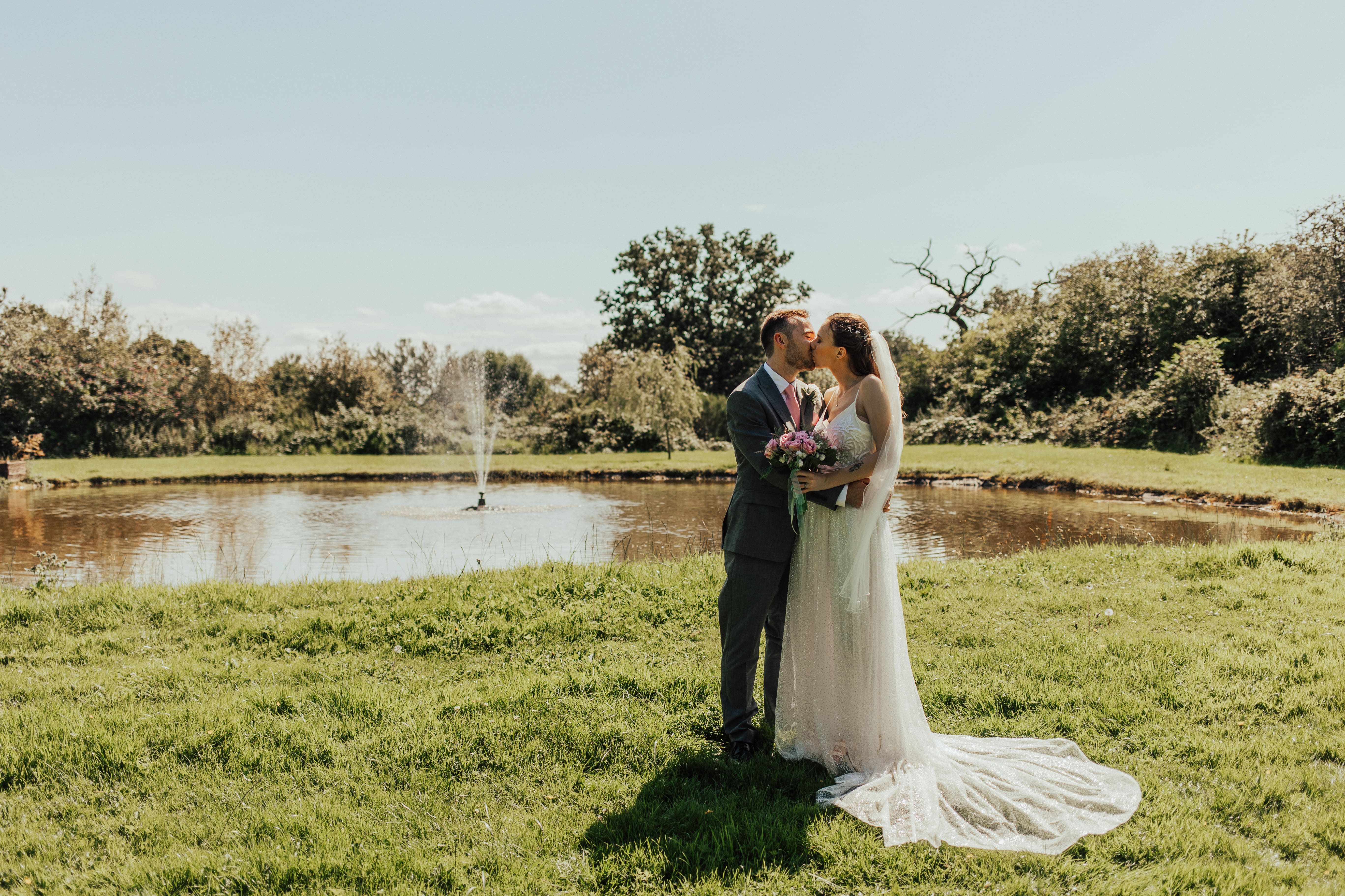 Bride and groom kissing by pond