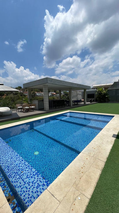 Outdoor pool with covered seating area and lush greenery.