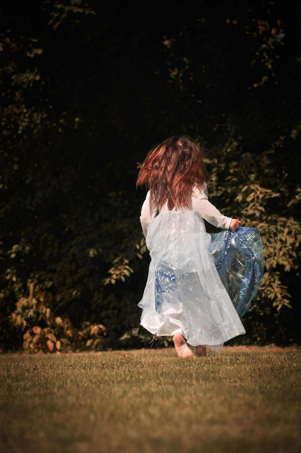 A little girl in a white dress is running in the grass