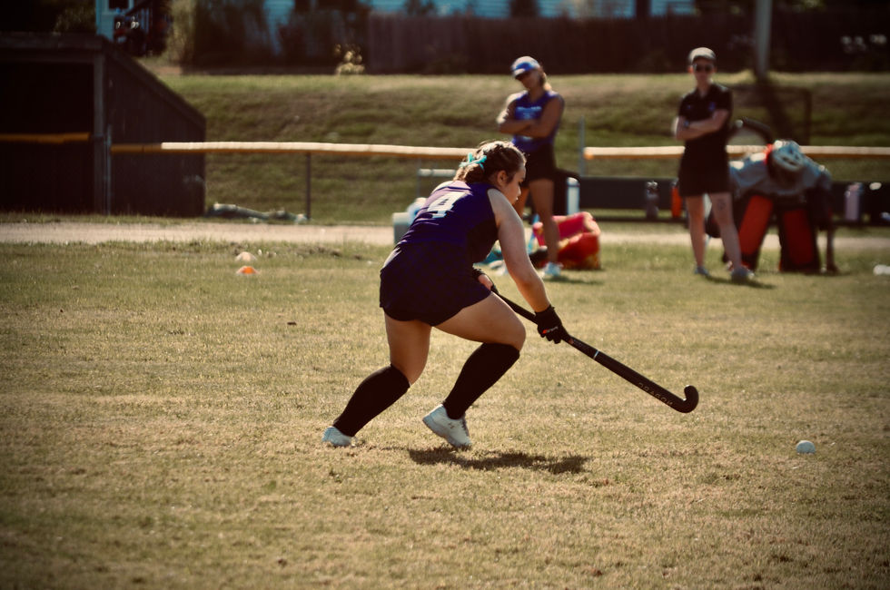 A girl in a purple shirt with the number 4 on it is playing field hockey