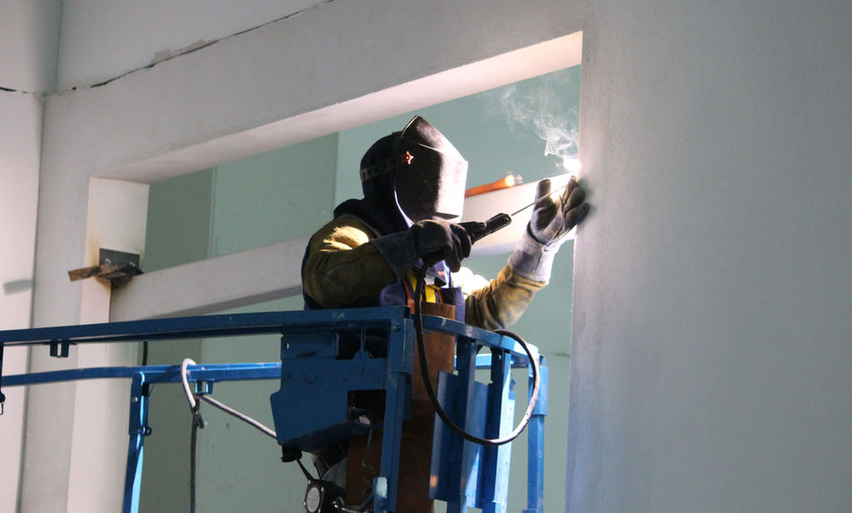 Soldador trabaja en construcción con equipo de seguridad, servicio herrería aluminio templados en México.