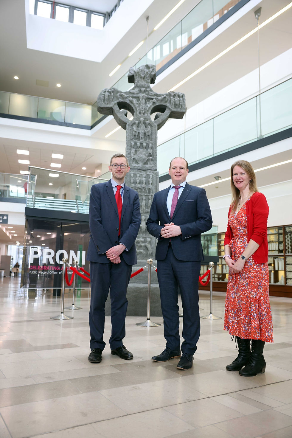 Communities Minister Gordon Lyons with Acting Director of PRONI David Huddleston and HERoNI’s Rhonda Robinson stand at the reconstructed Donaghmore high cross currently being exhibited at PRONI.