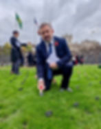Robin Swann MP placing a cross with a red poppy in the ground at the opening of the House of Commons Garden of Remembrance.