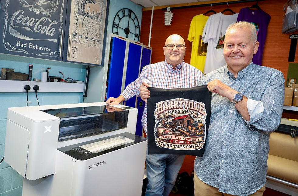 Stephen Reynolds, a Trustee at The Gallaher Trust holds up one of the t-shirts made by Harryville Mens Shed members as Denver McMeekin looks on.