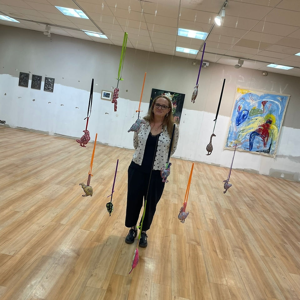 The artist standing by an art installation of multicoloured textile birds hanging from the gallery ceiling. 