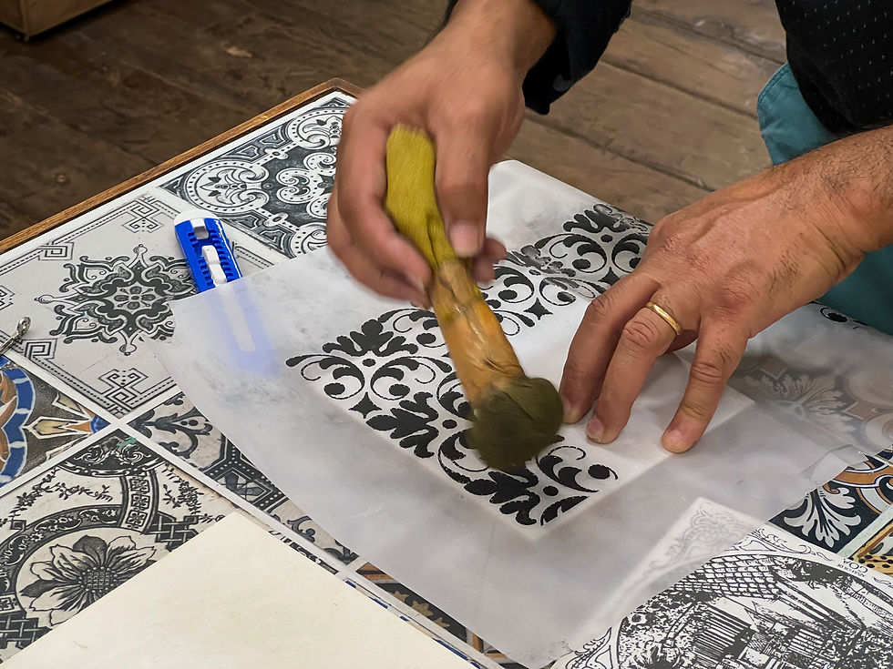 Hands stenciling a Azulejos pattern on white paper with a sponge on a patterned tabletop, focused craftwork scene