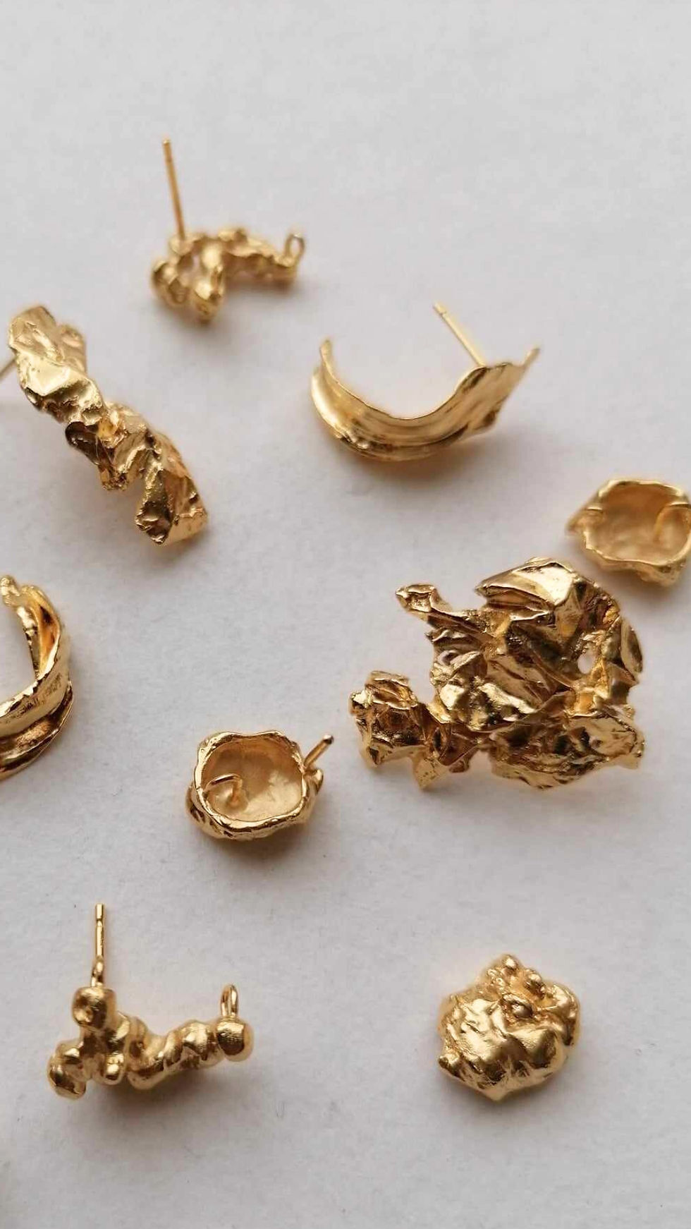 Assorted abstract gold earrings on a white background, each with a unique, irregular design, creating an artistic and luxurious look.