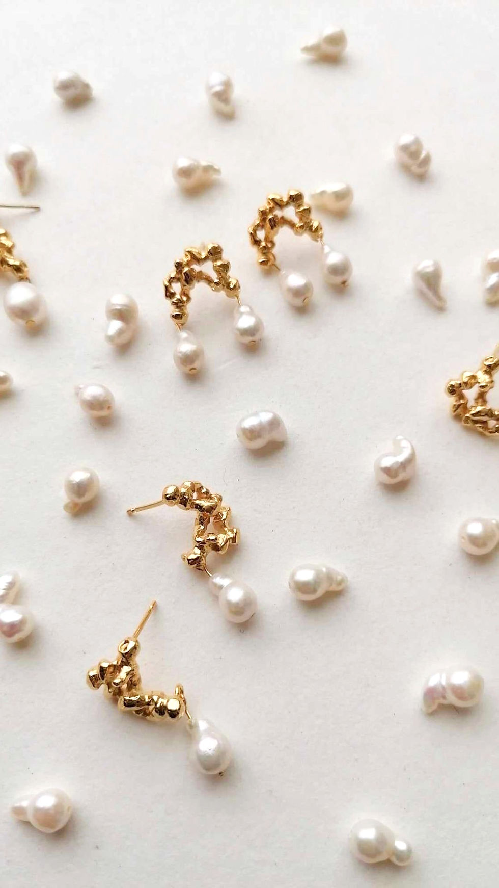 Gold earrings and scattered pearls on a pale surface, with a delicate and elegant arrangement.