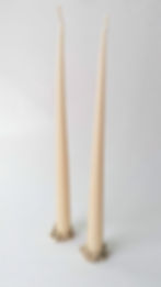 Two tall, cream-colored candles with intricate gold bases on a plain white background, creating a simple yet elegant scene.