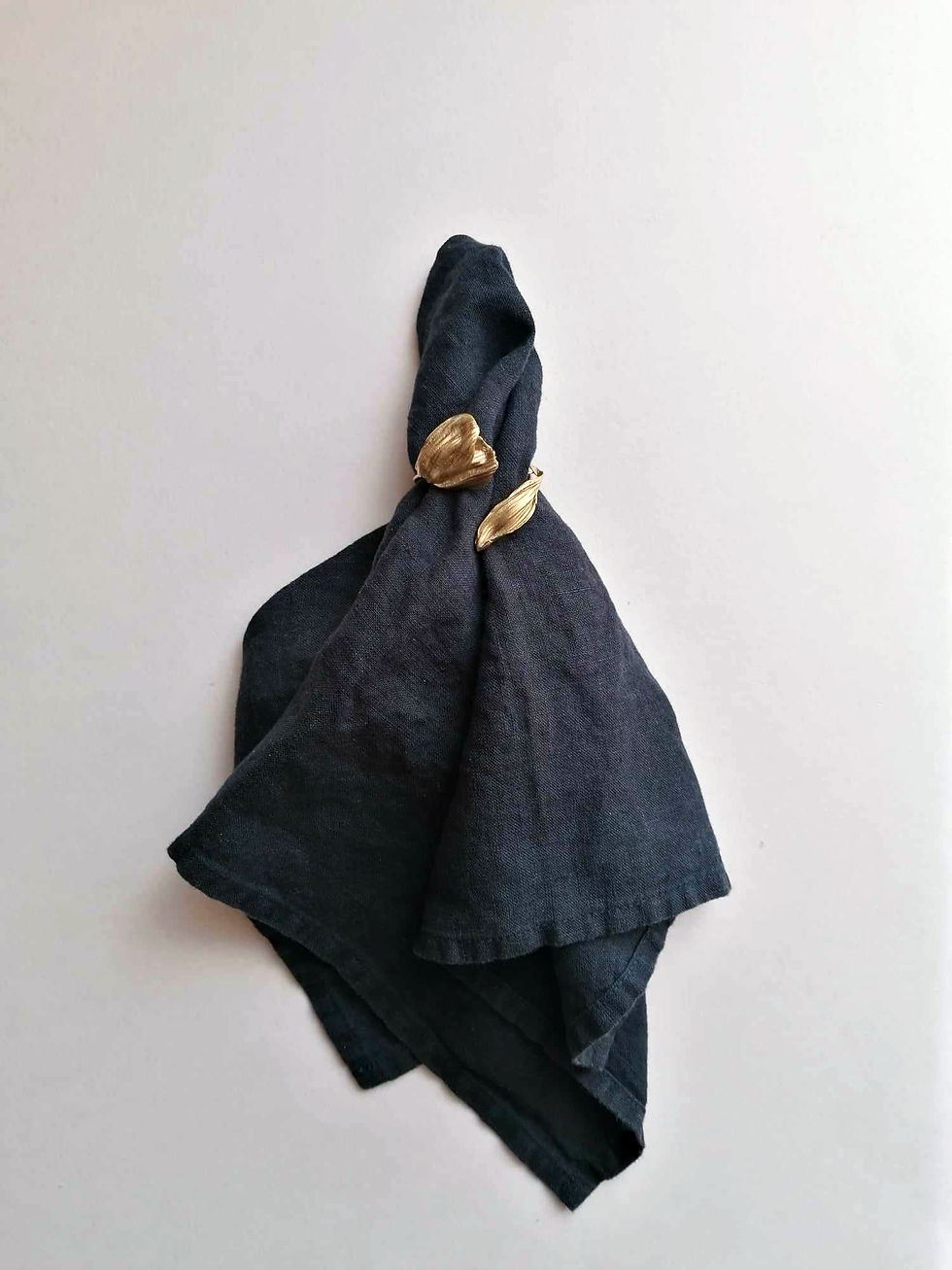 Dark blue napkin with gold leaf-shaped ring, set against a plain white background, creating an elegant and minimalist appearance.