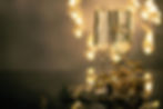 Two champagne glasses with gold ribbons and festive decorations on a reflective surface, set against a background of warm, blurred lights.