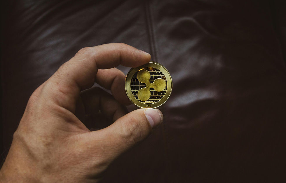 Hand holding a gold Ripple coin with a grid pattern over a dark, blurred background. The mood is focused and contemplative.