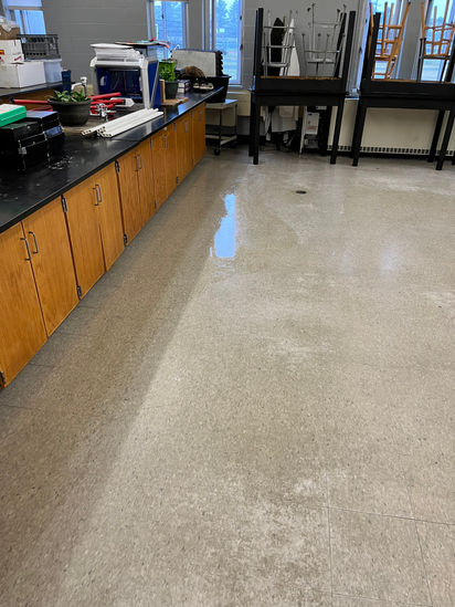 Shiny, wet lab floor beside cabinets and stacked classroom furniture.
