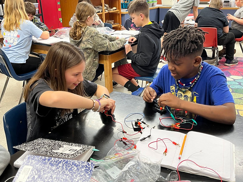 Two middle school students working on electrical circuits at a table.