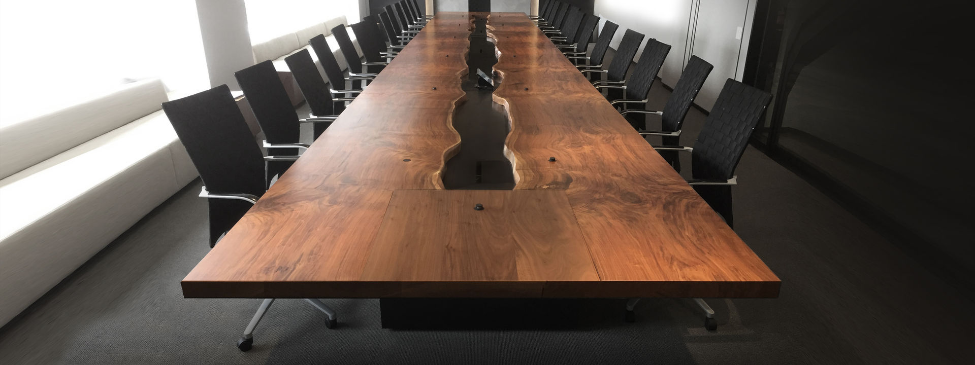 Made from four consecutive cuts of a live edge Walnut tree that had succumb to the twig beetle disease. The quadruple bookmatched piece inverts the live edge and allows the outer edges to be clean cut and functional. The center river is a blackened steel channel that houses five power ports with custom opening blackened steel doors. The microphones push down to mute and up to speak giving a voice to anyone seated at this massive 34' conference table.
