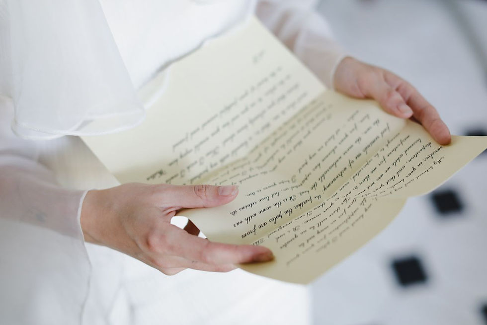 Hände in Weiß halten einen cremefarbenen handgeschriebenen Brief im weichen Licht.