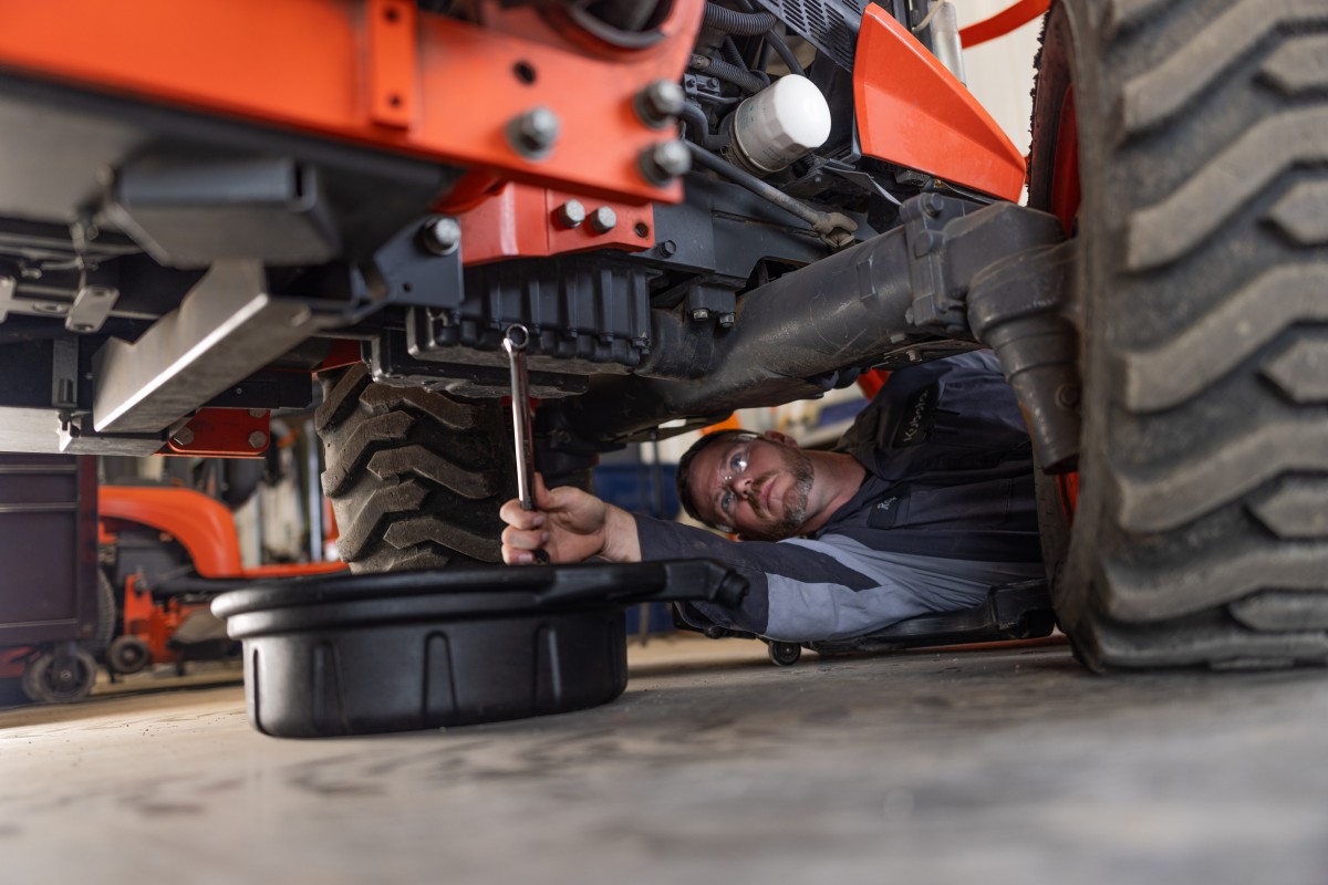 Diesel mechanic working underneath Kubota equipment during mobile service