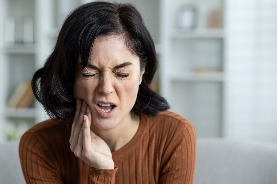 Woman with short dark hair and brown top holding her cheek in pain, indicating a severe to