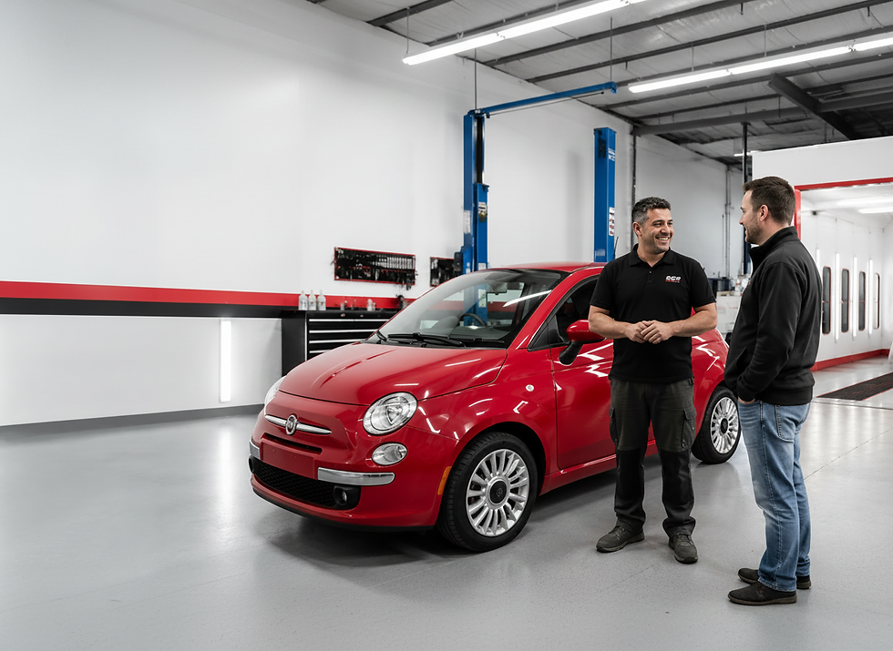Two men discussing a red car in a car body shop.