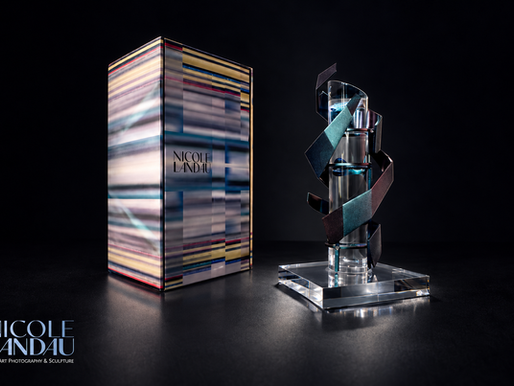 Nicole Landau statue on a clear base beside a striped box, set against a dark studio background. Artist Nicole Landau, Ascent, A Totem of Flight. The Fine Art Ledger. Corporate Award.