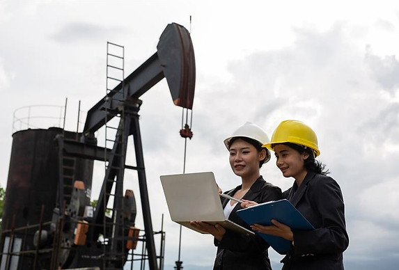 Two female engineers stand beside working oil pumps with a white sky__.jpg