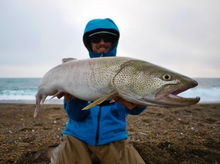 Smiling angler holding a Japanese Taimen in front of crashing waves on the coast of Hokkaido.