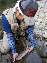 Fly fisherman releasing a rainbow trout into a natural river in Hokkaido, Japan.