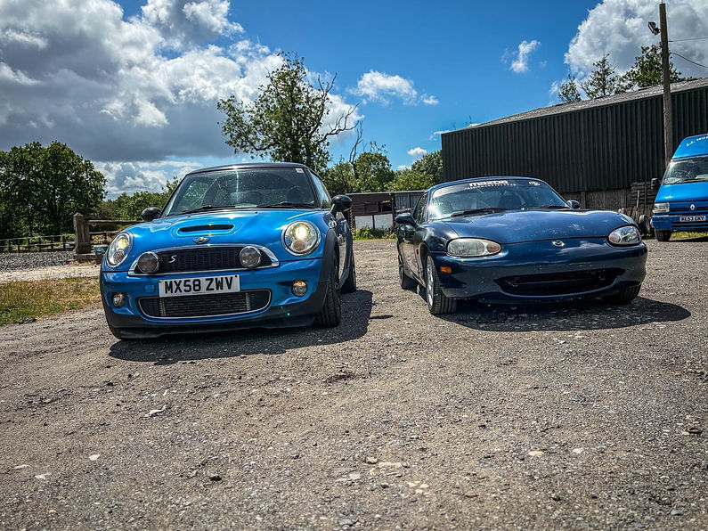 Mini Cooper and Mazda sports car sitting outside on driveway in countryside