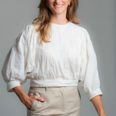 Corporate headshot — portrait in white top and trousers, neutral studio