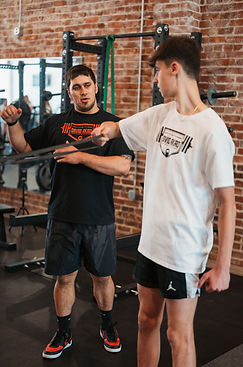 A personal trainer coaching his high school athlete on a shoulder mobility drill.