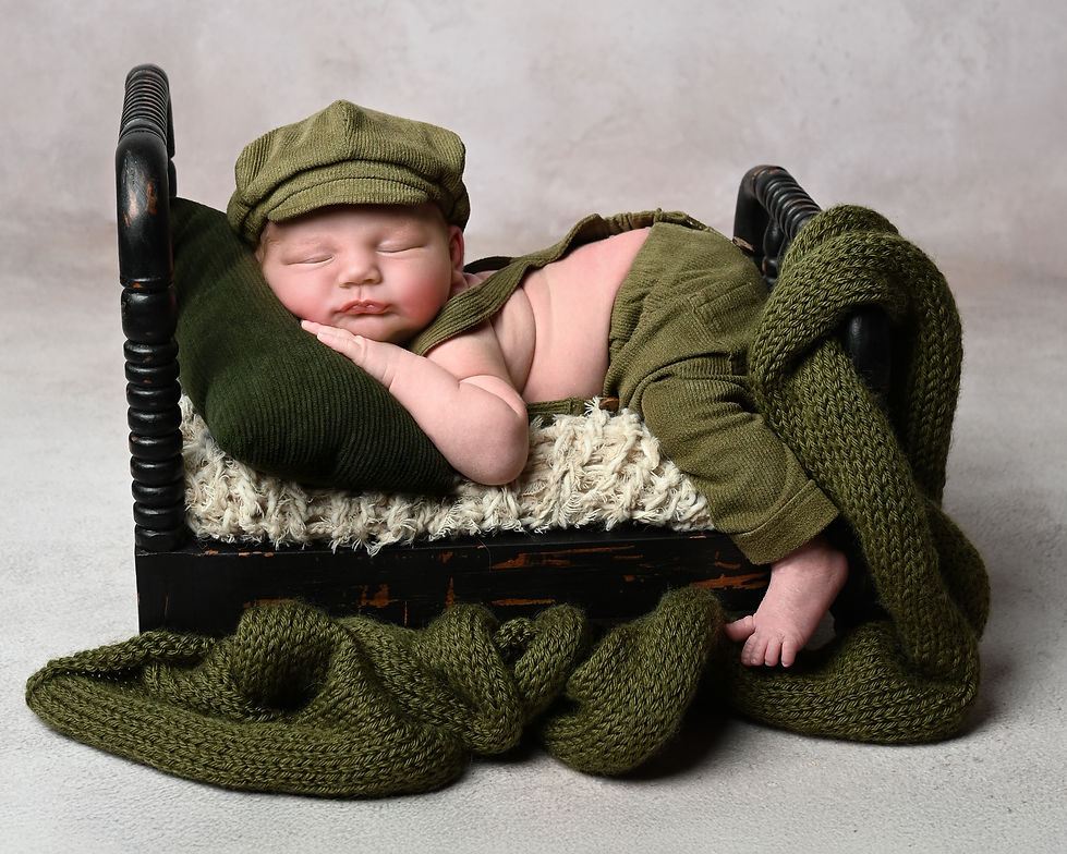 Newborn Photography Session in Buckeye Arizona with a little baby boy in a green outfit laying on a bed